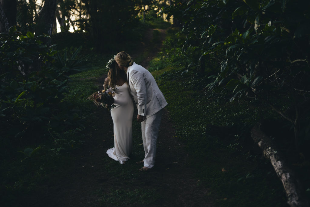Bride and groom kiss in Hawaiian forest